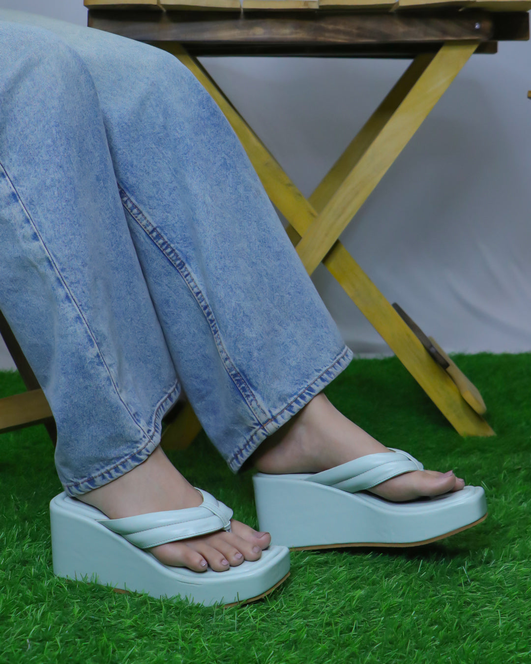Blue open-toe vegan leather wedge slides with a simple strap, 3-inch heel, worn with blue jeans on a green grass surface