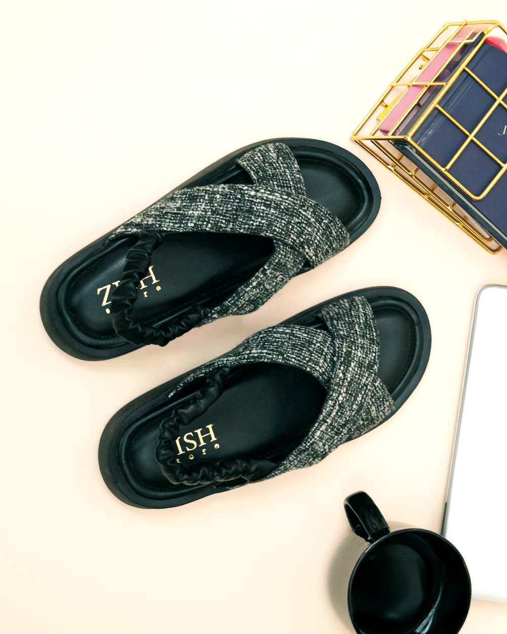 Black tweed criss-cross sandals with cushioned black insoles and elastic back straps on a light background with accessories