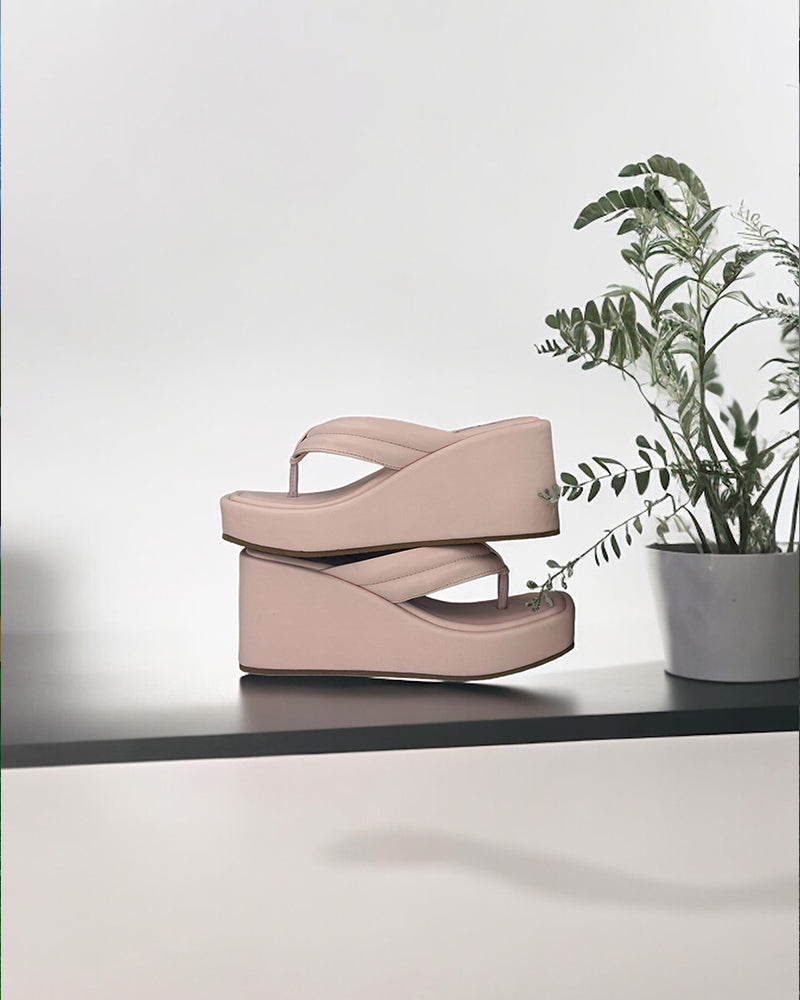 Pink wedge slides with open toe, 3-inch heel, and simple strap design on black surface next to potted plant